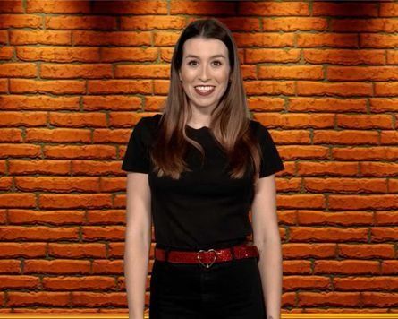 Una mujer con una camisa negra está parada frente a una pared de ladrillos.