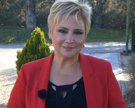 Una mujer que lleva una chaqueta roja y una camiseta negra sonríe a la cámara.