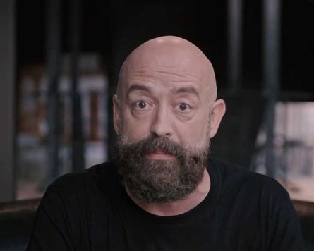 Un hombre calvo con barba y bigote lleva una camisa negra.