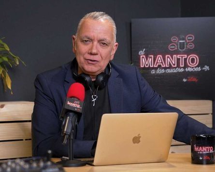 Un hombre está sentado en una mesa con una computadora portátil y un micrófono.