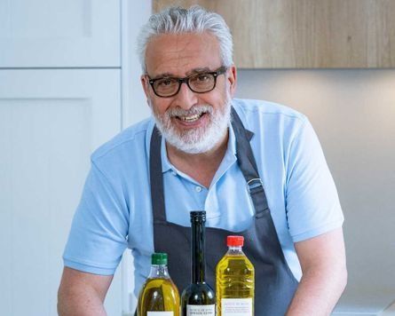 Un hombre con delantal sostiene tres botellas de aceite de oliva.