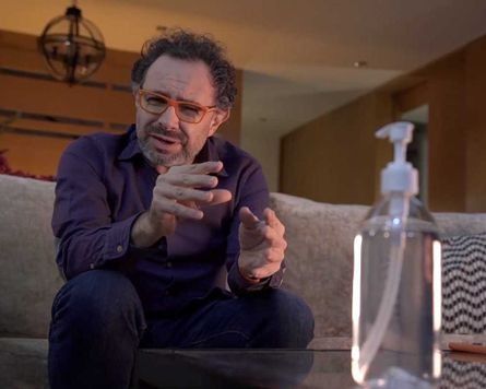 Un hombre está sentado en un sofá junto a una botella de desinfectante de manos.