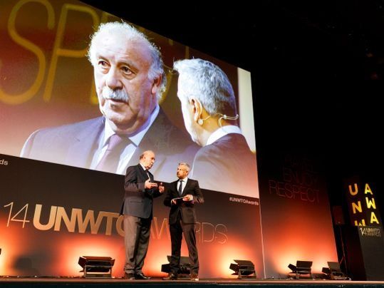 Dos hombres están de pie frente a una pantalla grande que dice 14 premios OMT