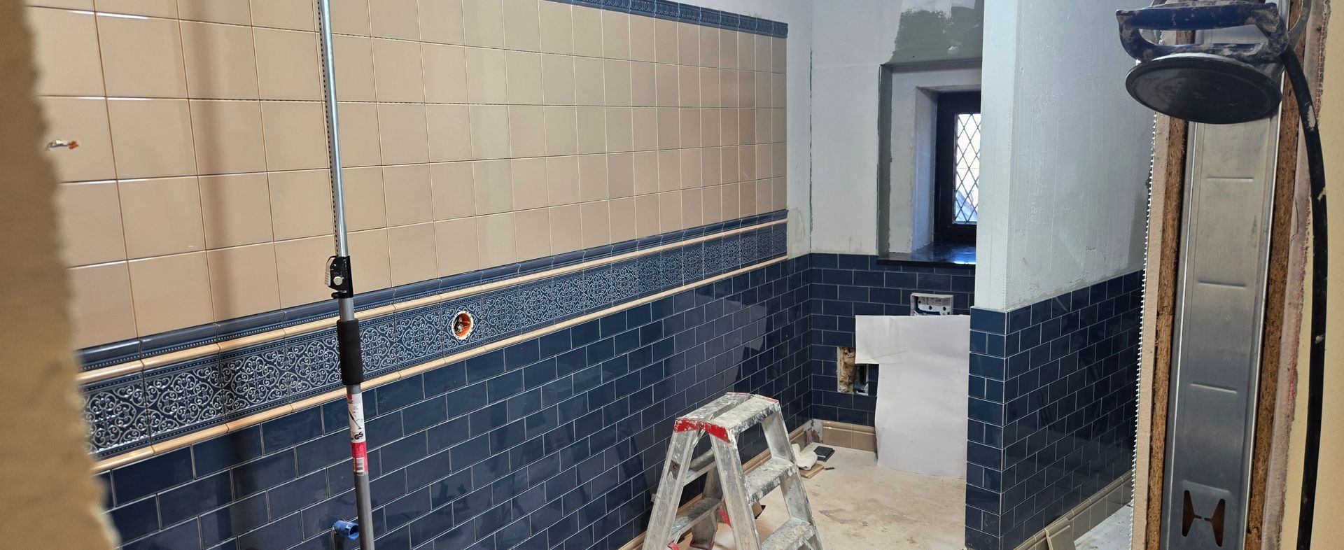 Ein im Bau befindliches Badezimmer mit blauen und weißen Fliesen und einer Leiter.