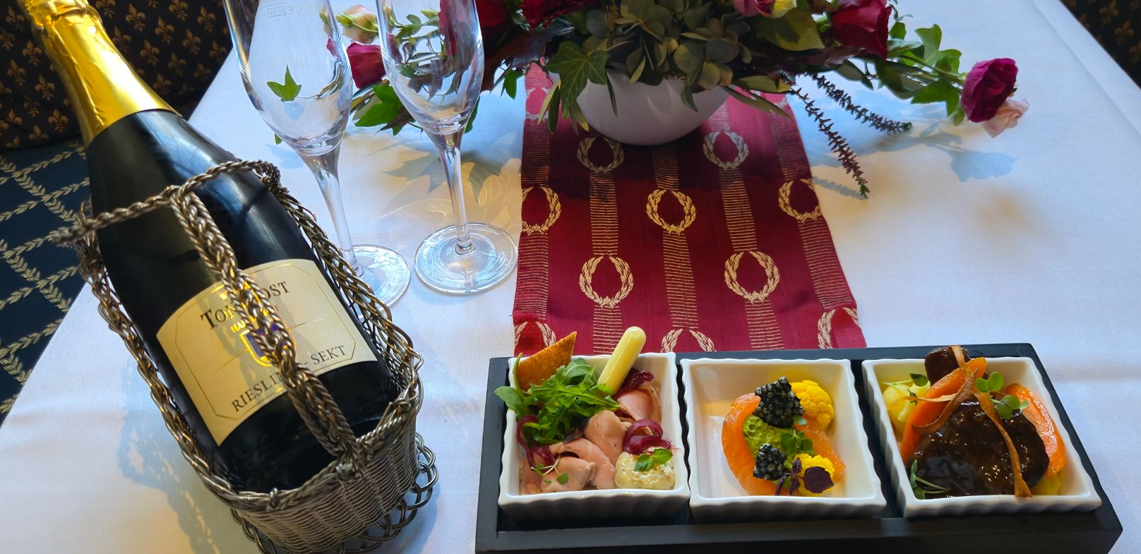 Romantische Tischdekoration: Flasche Champagner in einem silbernen Halter, Speisen in kleinen Schälchen, Blumen und Gläser.