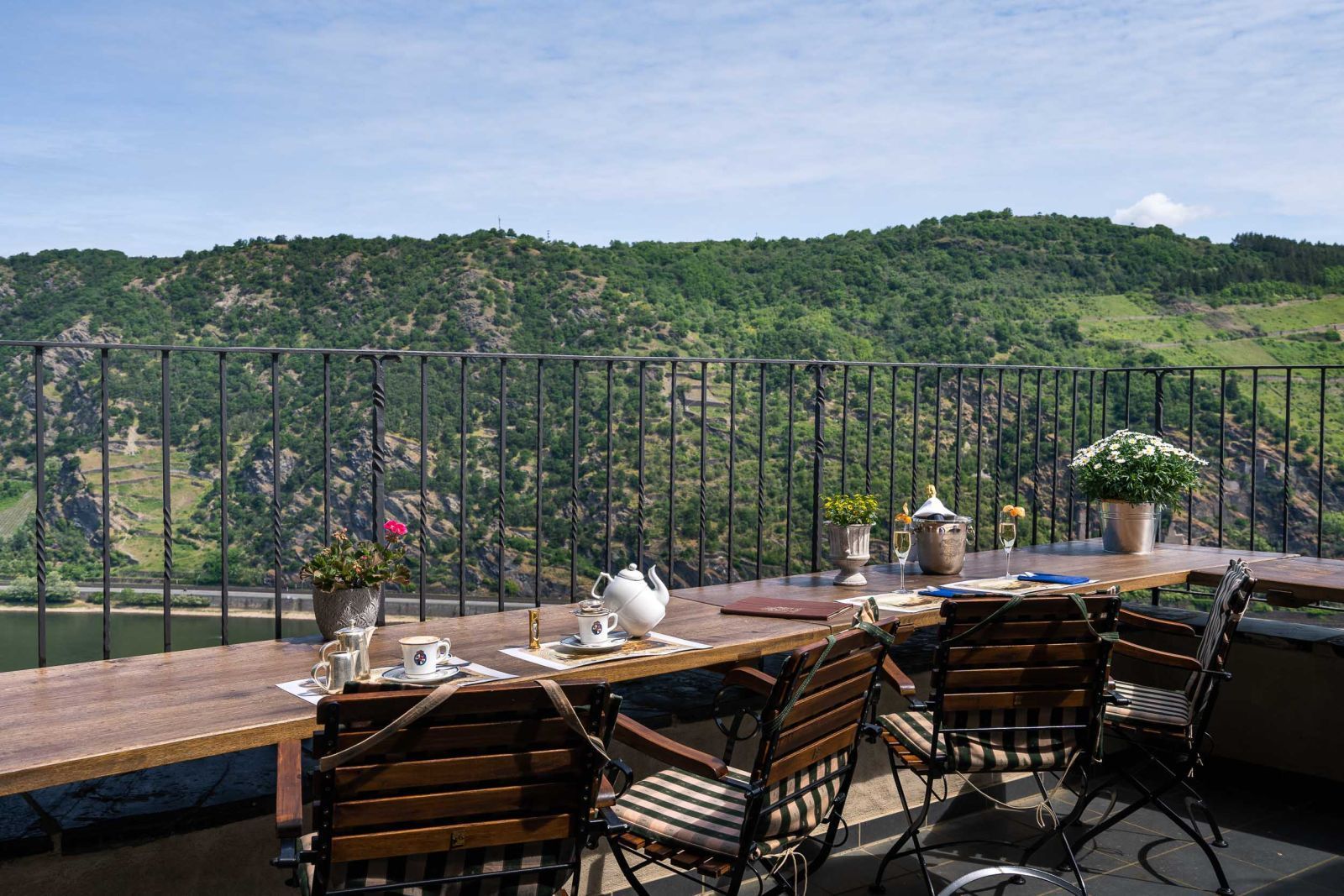 Ein Tisch und Stühle auf einem Balkon mit Blick auf einen Fluss und Berge. Bistro Terrasse