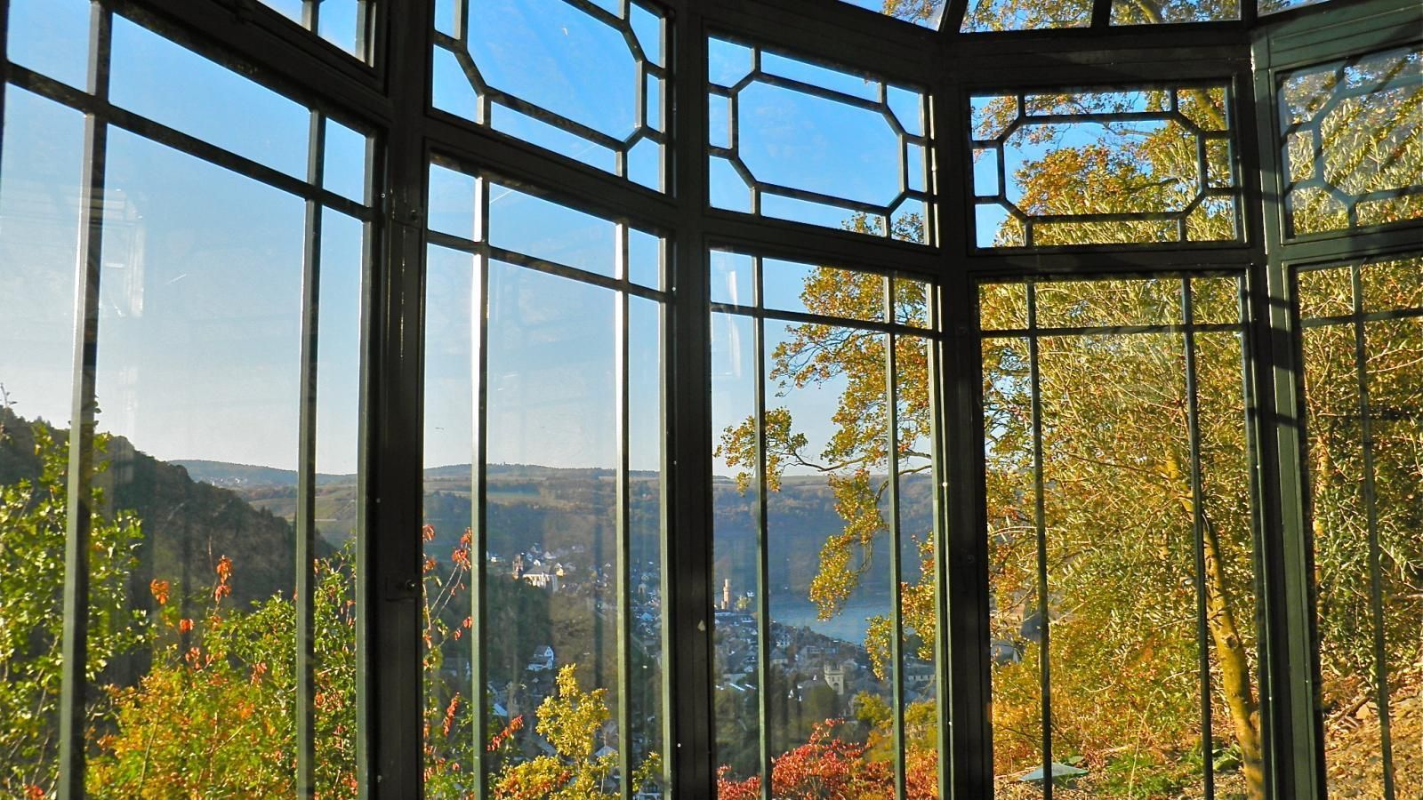 Ein Raum mit vielen Fenstern und Blick auf Bäume und ein Gewässer.