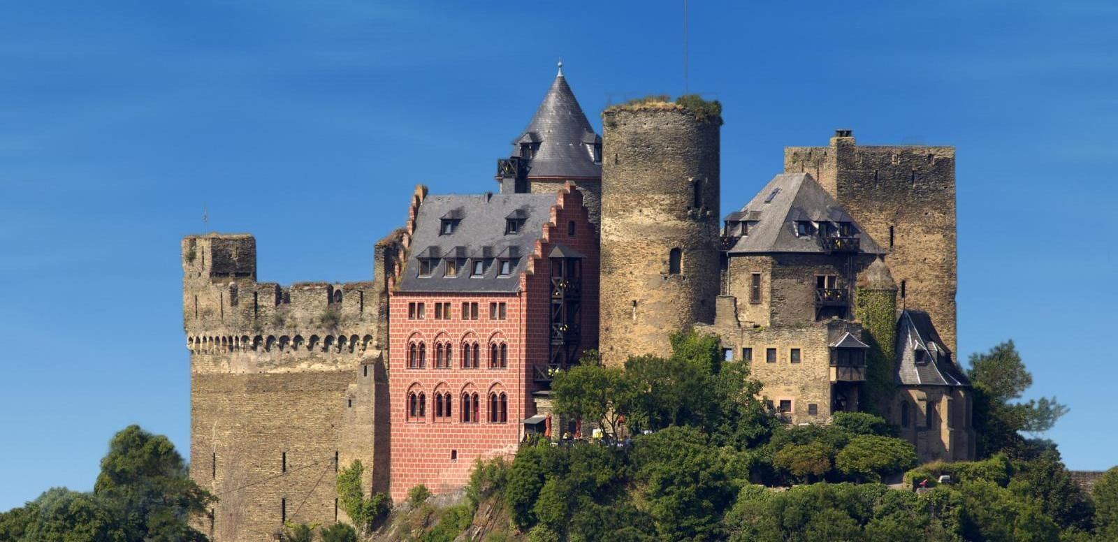 Auf einem Hügel, umgeben von Bäumen, steht eine große Burg.