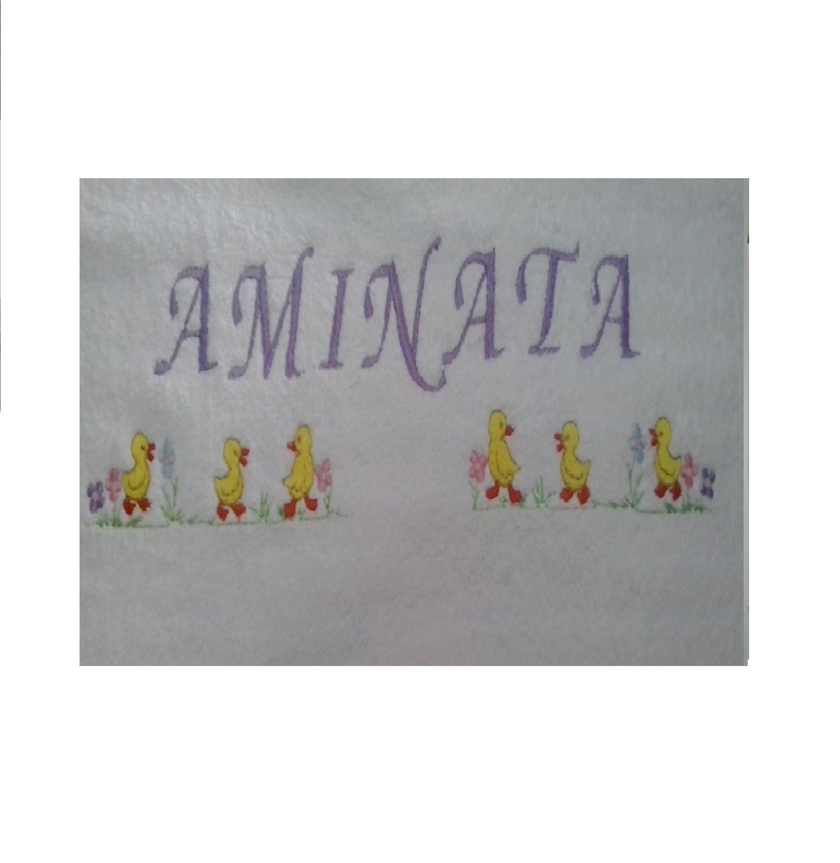 Letrero decorativo con la inscripción “AMINATA” y pequeñas figuras amarillas de dibujos animados en la parte inferior sobre un fondo blanco.