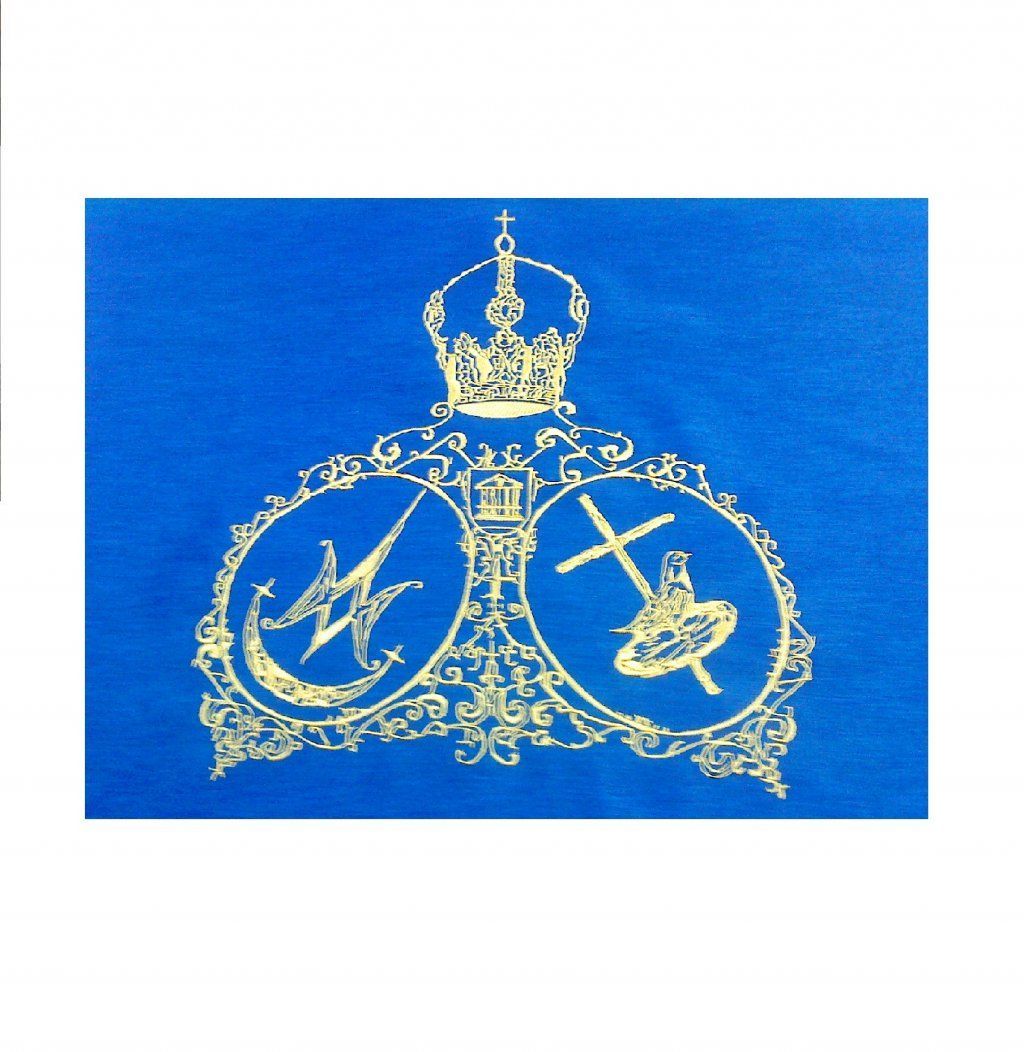 Emblema de doble círculo bordado en oro con corona sobre tela azul, con herramientas cruzadas y adornos decorativos.