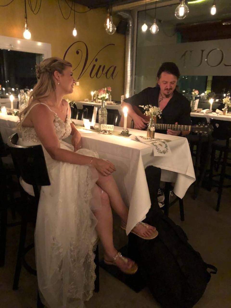 Braut sitzt an einem Tisch, während ein Mann Gitarre spielt. Foto von der Viva Bar & Lounge