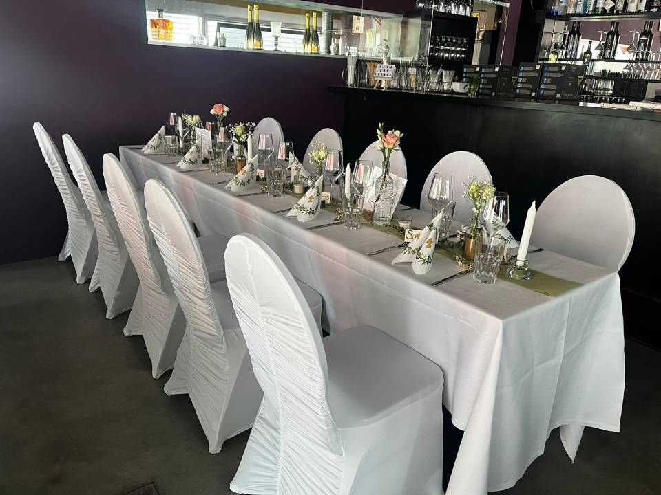 Ein langer Tisch mit weissen Stühlen und einer weissen Tischdecke. Foto der Viva Bar & Lounge