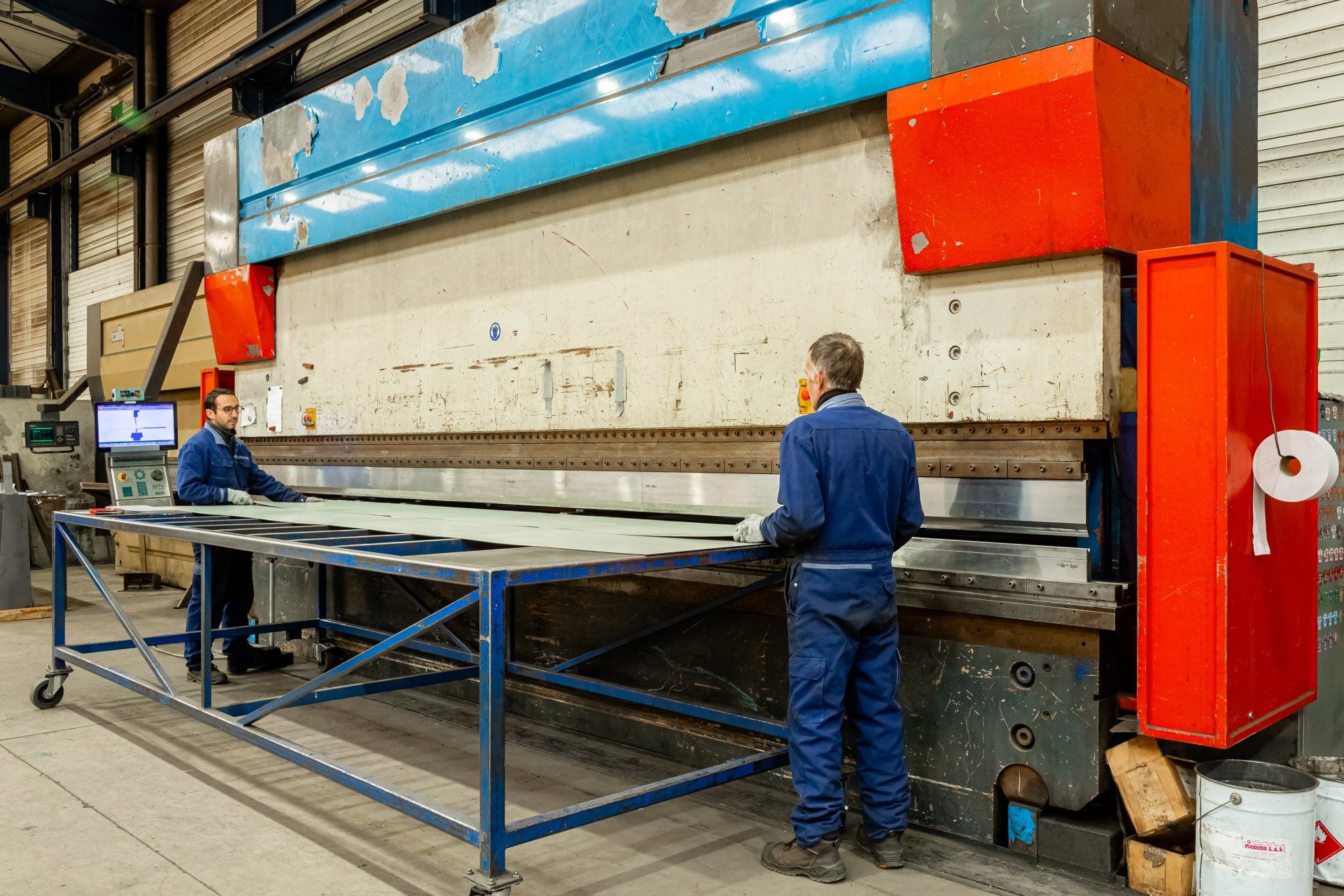 Deux hommes travaillent dans un atelier et tiennent une plaque de métal