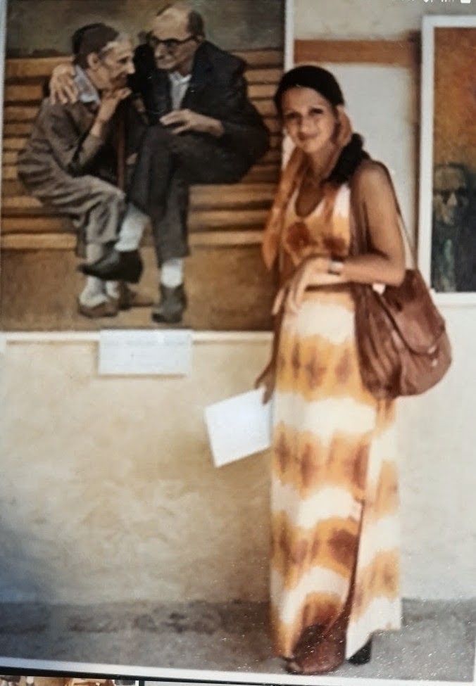 Una mujer vestida de naranja y blanco está de pie junto a una vitrina con dos figuras sentadas.