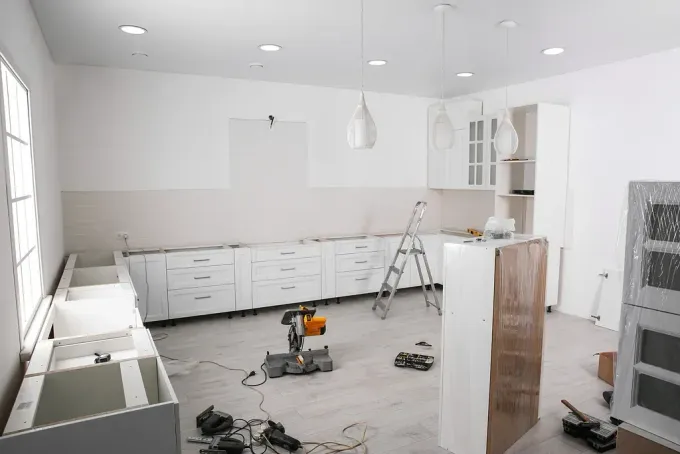 Cocina en remodelación, gabinetes blancos, herramientas, escalera y escombros de construcción.