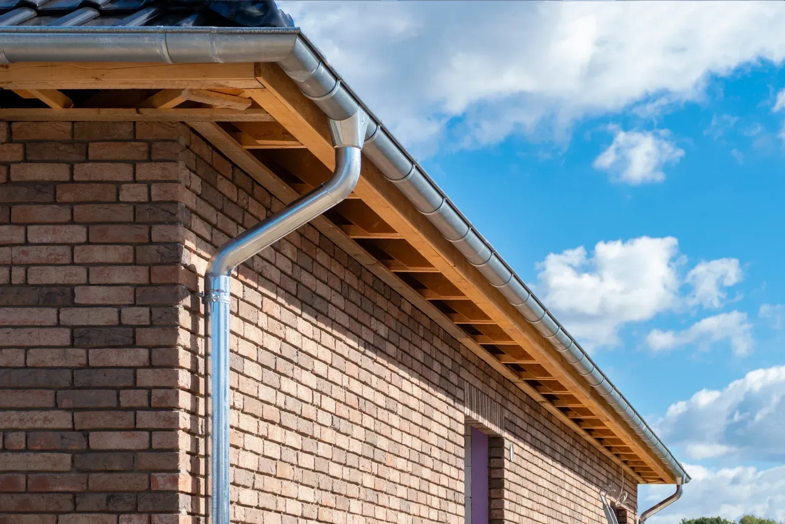 Brick house exterior with a metal gutter under a slanted roof against a blue sky
