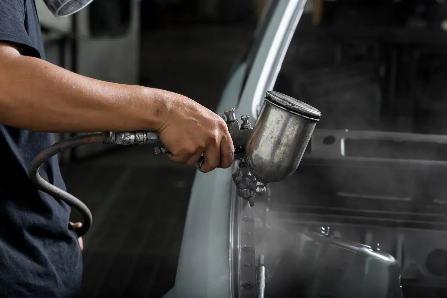 En un taller, una persona utiliza una pistola de pintura en aerosol para aplicar pintura al chasis de un vehículo.