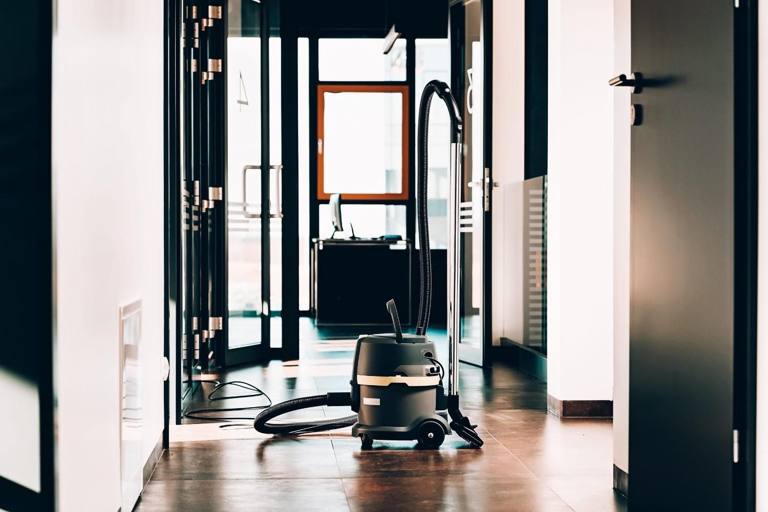 Aspiradora en un pasillo con puertas y una ventana luminosa al fondo.