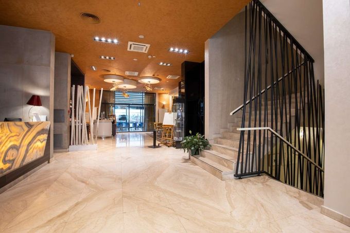 Vestíbulo moderno con techo de madera, suelo de mármol, mostrador de recepción y escalera con barandilla negra.