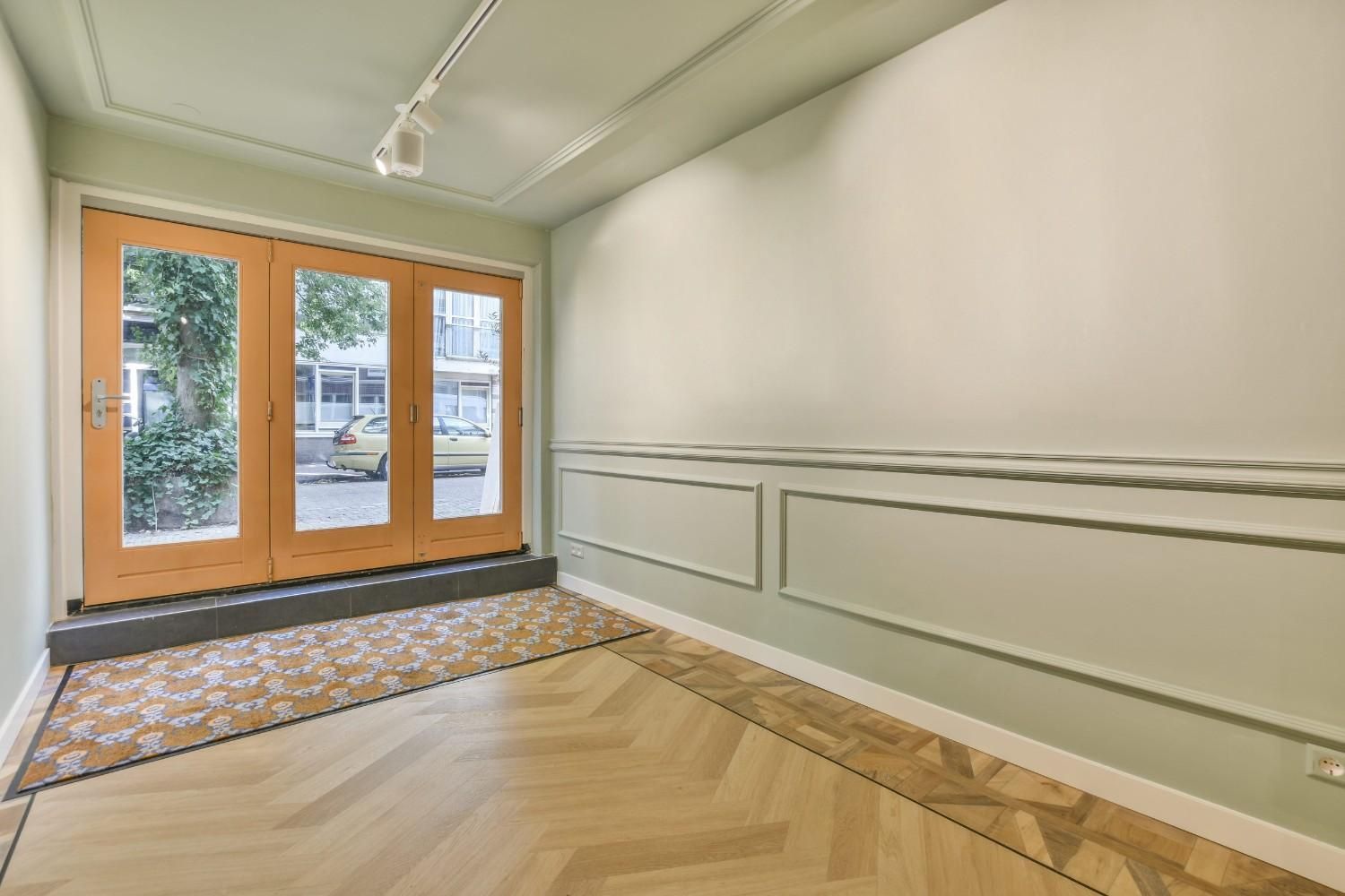 Pasillo vacío con puertas francesas, paredes blancas y suelo de madera en espiga.