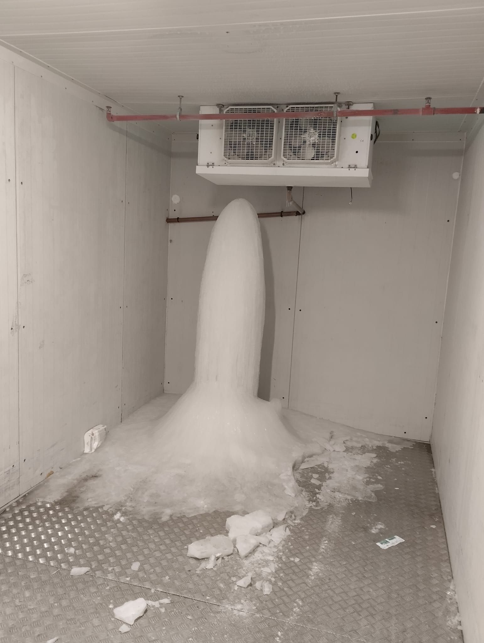 Une imposante colonne de glace s'élève du sol d'une chambre froide située sous un groupe frigorifique fixé au plafond.