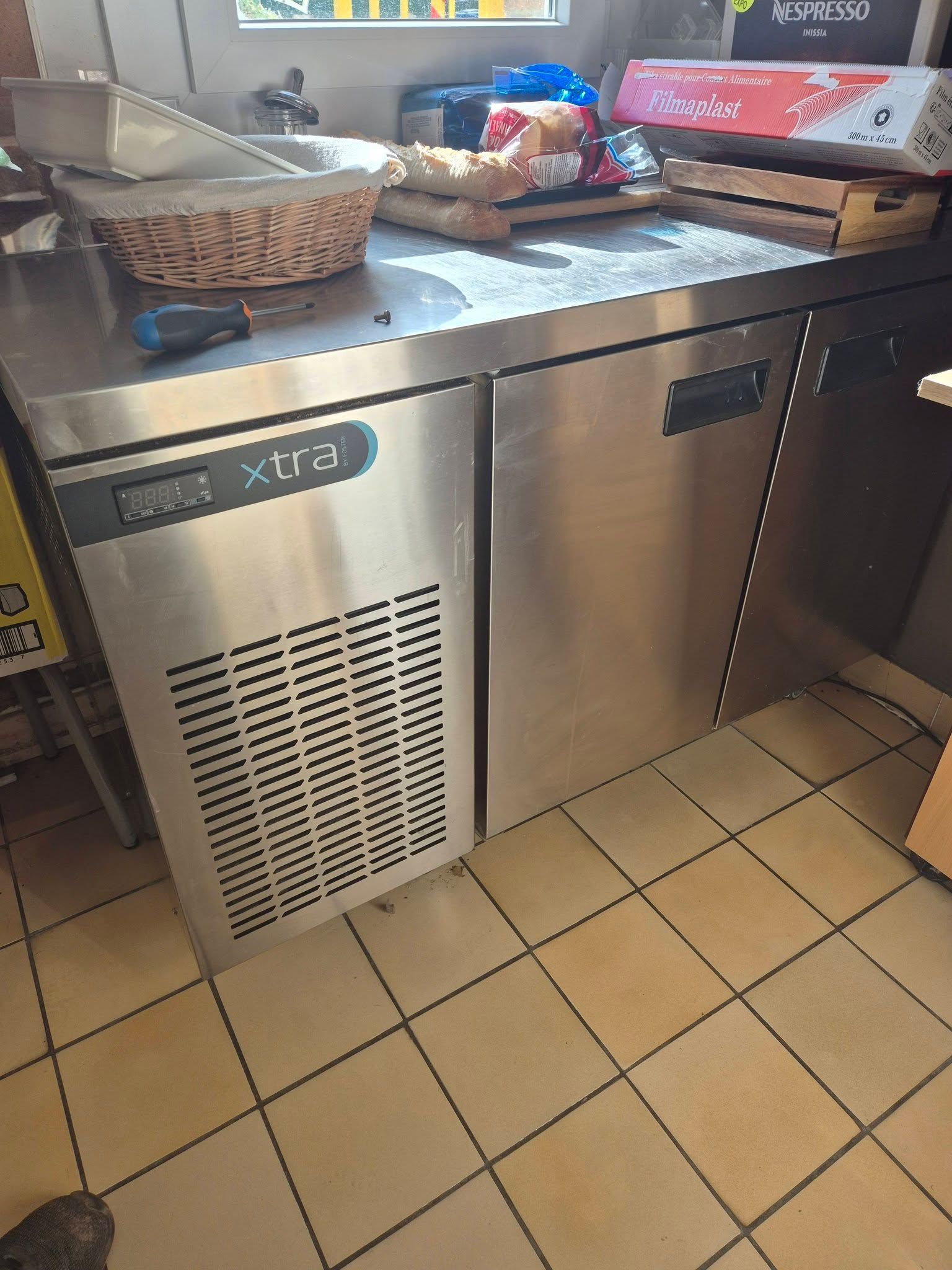 Un réfrigérateur commercial sous comptoir en acier inoxydable, à deux portes et à panneau avant ventilé, dans une cuisine.