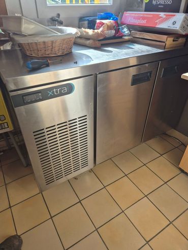 Un réfrigérateur commercial sous comptoir en acier inoxydable, à deux portes et à panneau avant ventilé, dans une cuisine.