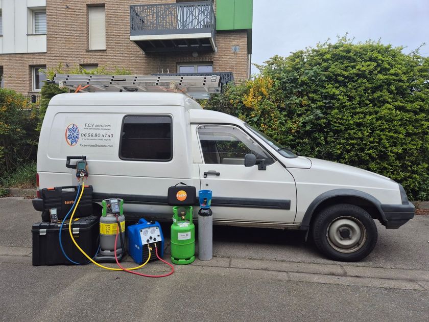 Une camionnette utilitaire blanche est garée dans une rue, avec du matériel spécialisé et des bonbonnes de gaz disposées au sol à côté.