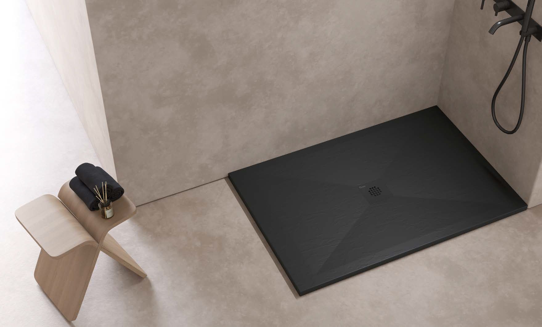 Un plato de ducha negro está en el suelo de un baño al lado de un taburete de madera.