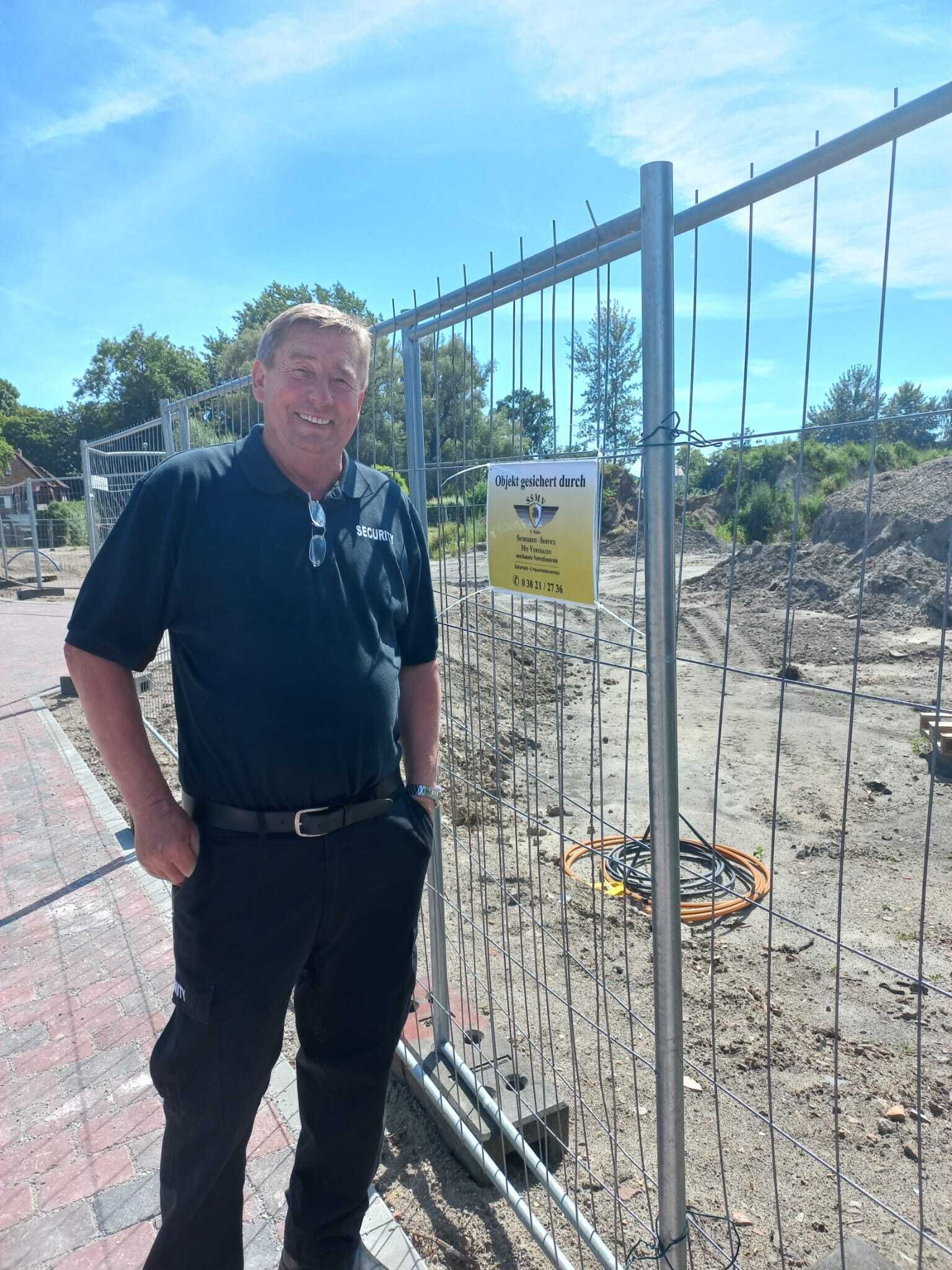 Ein Mann steht vor einem Zaun, an dem ein Schild hängt.