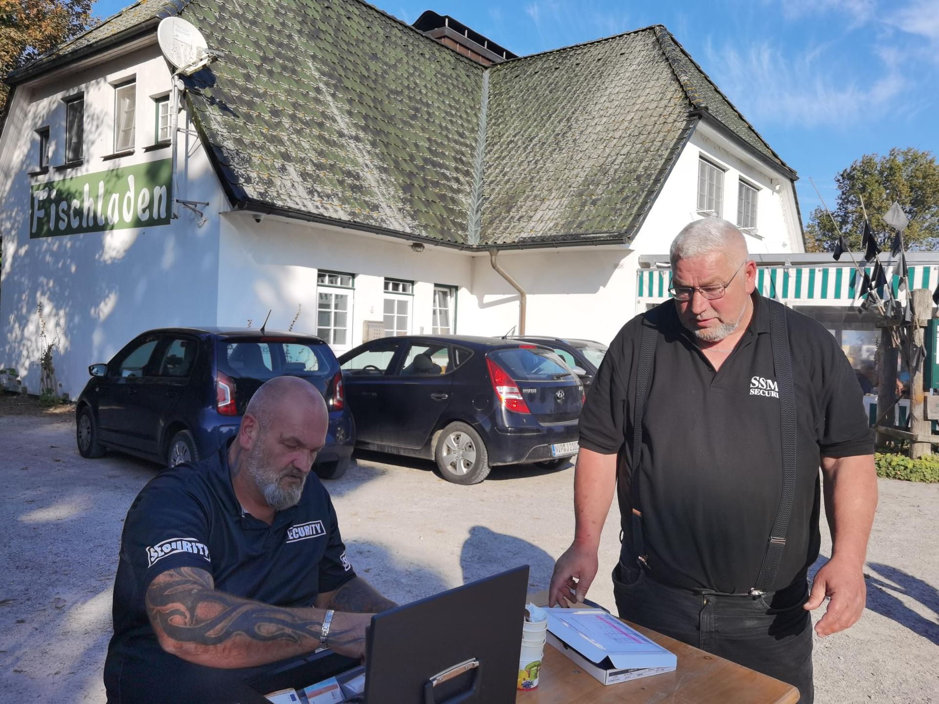 Zwei Männer stehen vor einem Gebäude mit einem Schild mit der Aufschrift „Fleischladen“