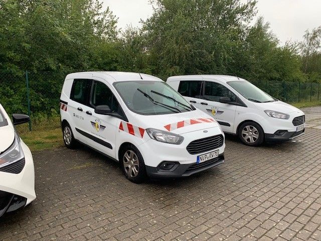 Drei weiße Lieferwagen stehen nebeneinander auf einem Ziegelsteinpflaster.