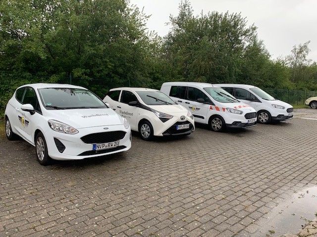 Eine Reihe weißer Autos und Lieferwagen steht auf einem Parkplatz.