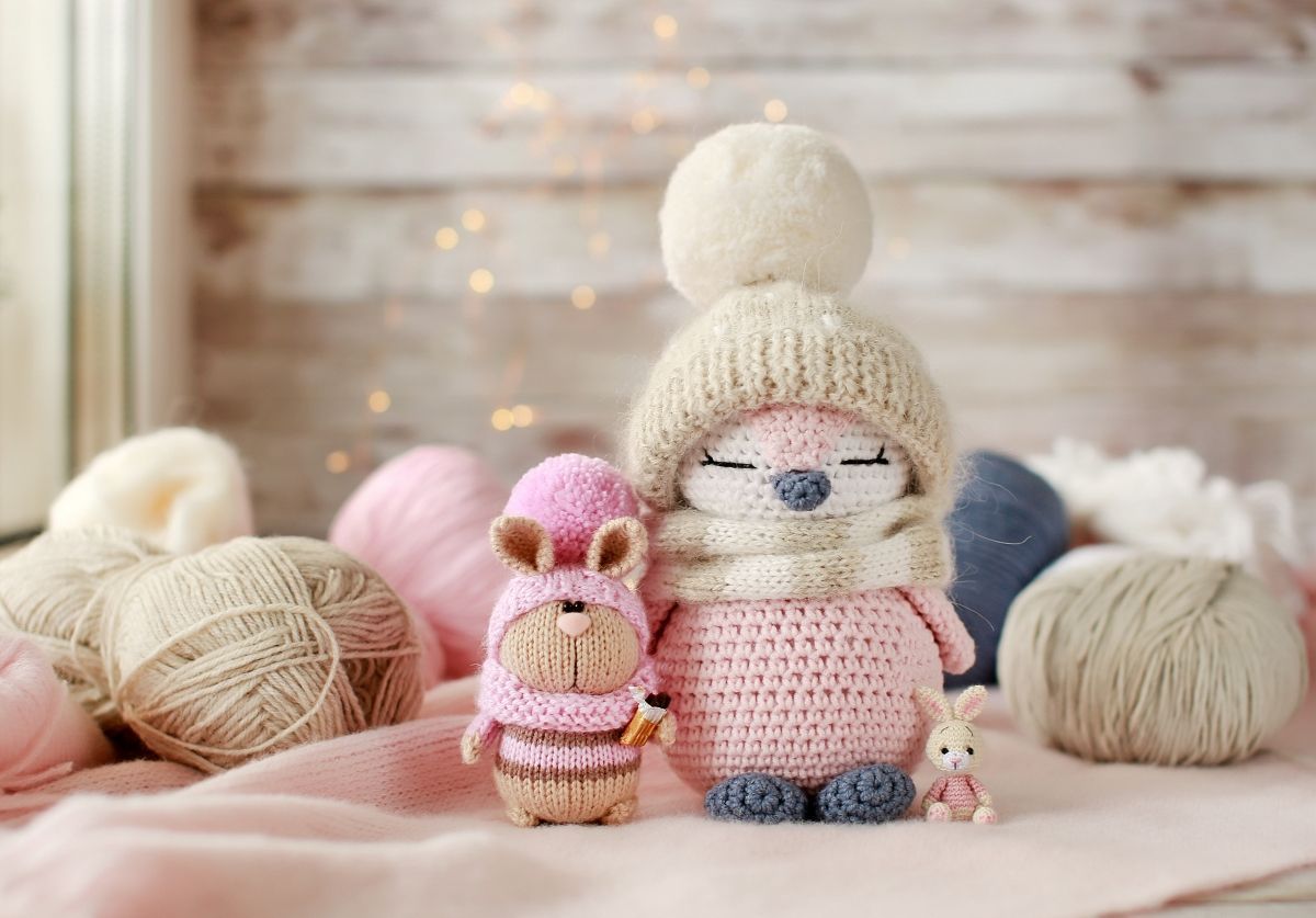 Figuras de pingüinos y conejos tejidos a ganchillo con gorros y bufandas de invierno, junto a la lana.