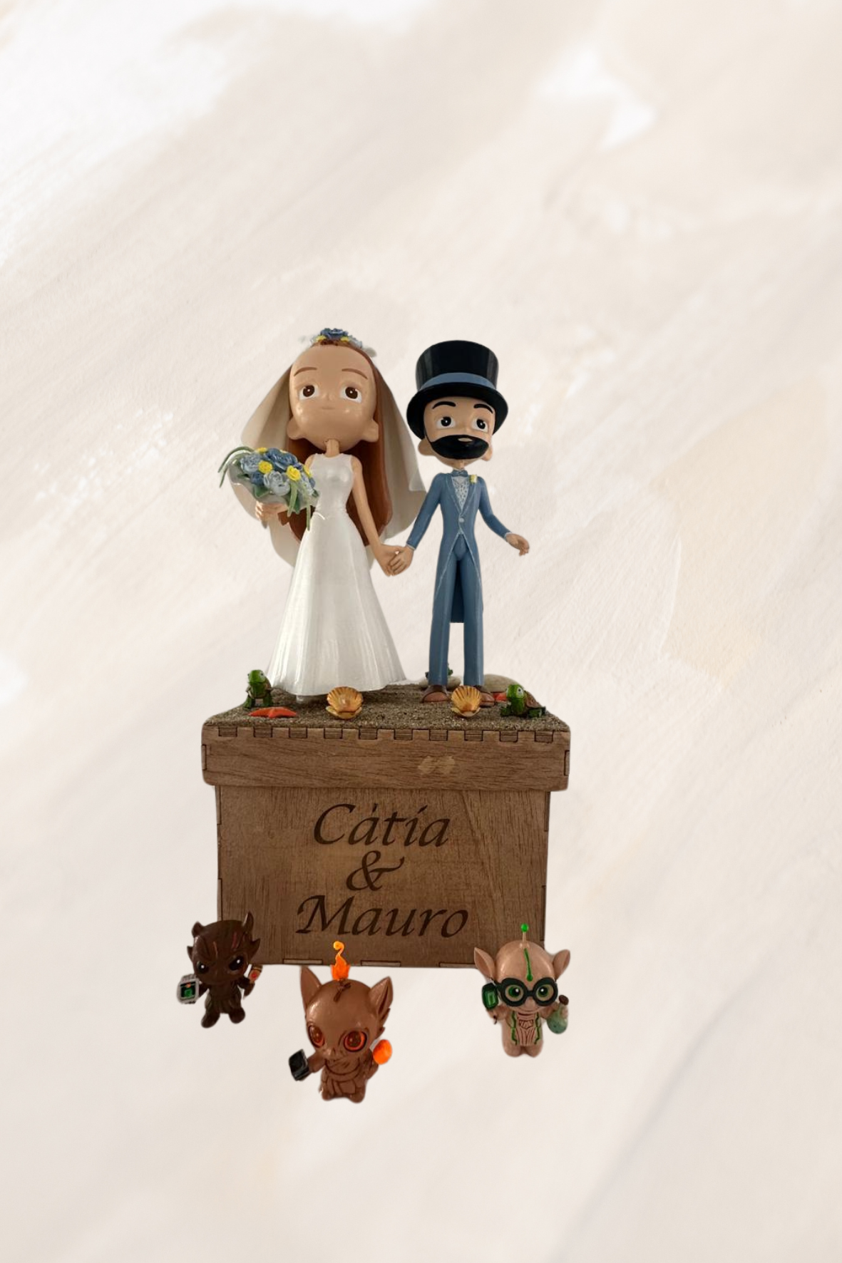 Adorno para tarta nupcial con novia, novio y criaturas fantásticas; el texto dice 