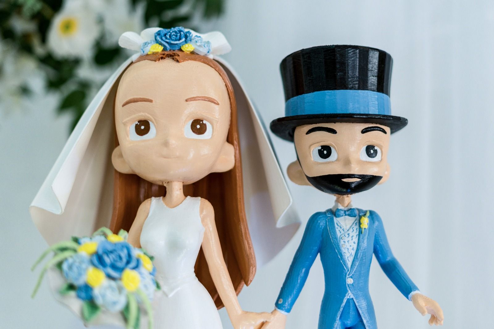 Figura para tarta nupcial de una novia y un novio; ella sostiene un ramo, él lleva un traje azul y un sombrero de copa.