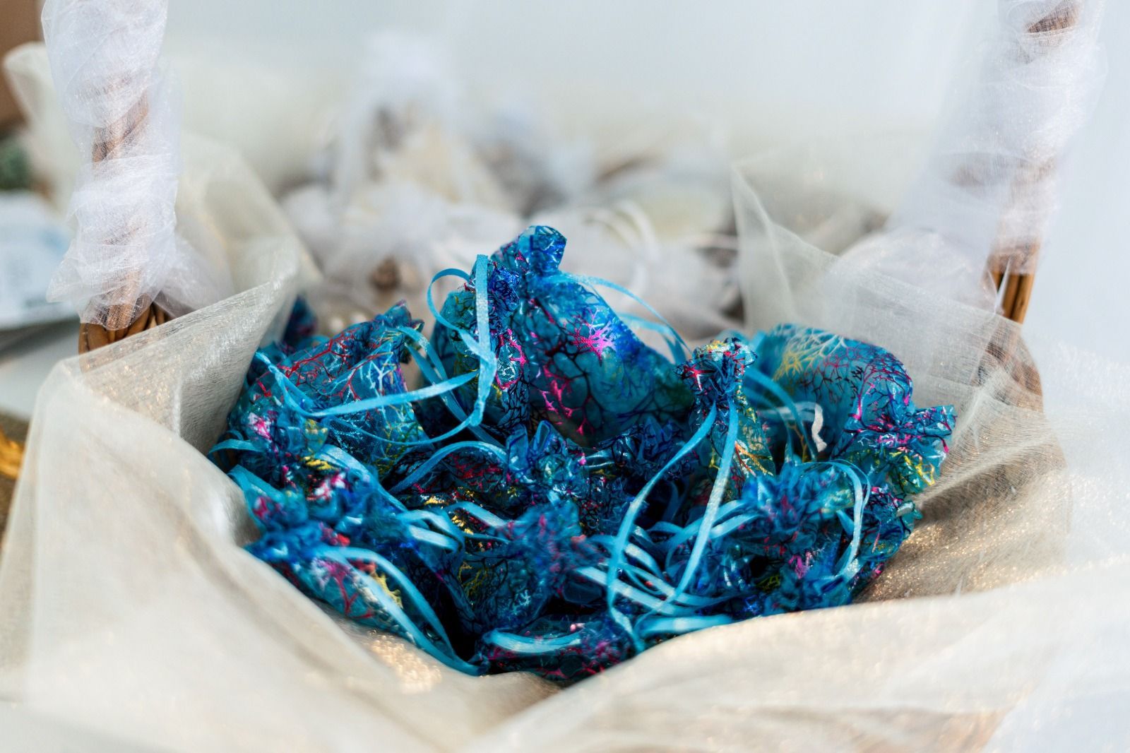 Cesta de obsequios para fiestas, azul y brillante, envuelta en tul blanco.