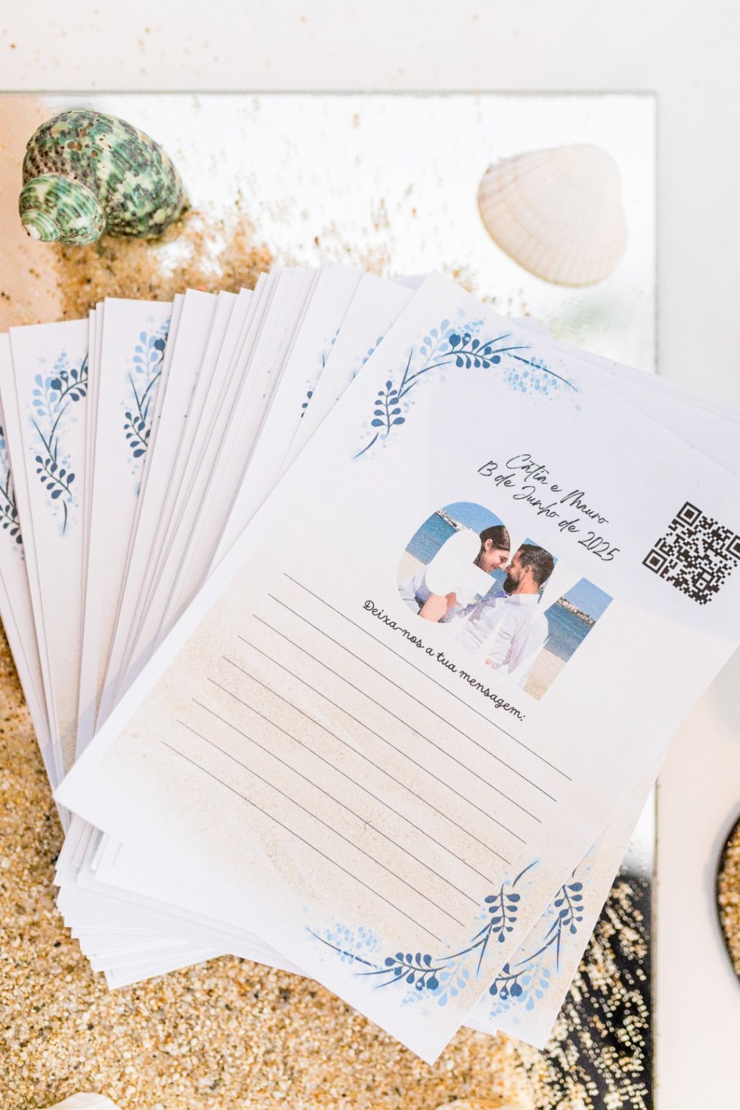 Pila de libros de firmas de boda blancos con la foto de dos hombres, sobre arena con conchas.