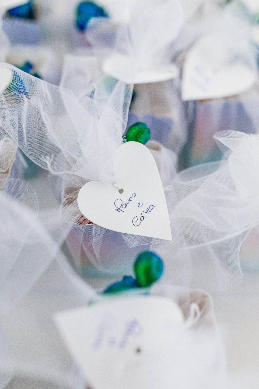 Pequeños detalles de boda con etiquetas en forma de corazón, atados con tul blanco y cuentas azules.