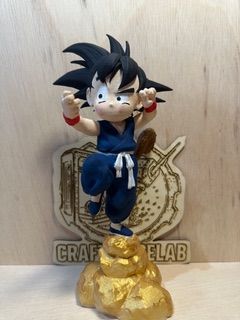 Figura de Goku en pose de combate, de pie sobre una nube dorada, frente a un logotipo grabado en madera.