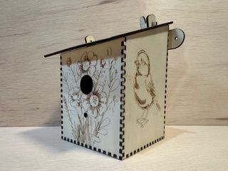 Casita para pájaros de madera con grabados de flores y pájaros, techo inclinado.