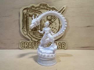 Estatua blanca de una persona con un dragón enroscado a su alrededor; letrero de madera de Craft Lab al fondo.