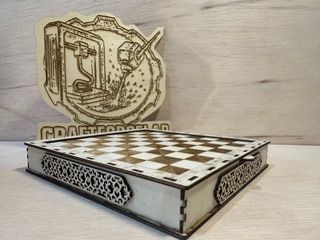Juego de ajedrez de madera con laterales ornamentados grabados y tapa del tablero, colocado frente a un logotipo.