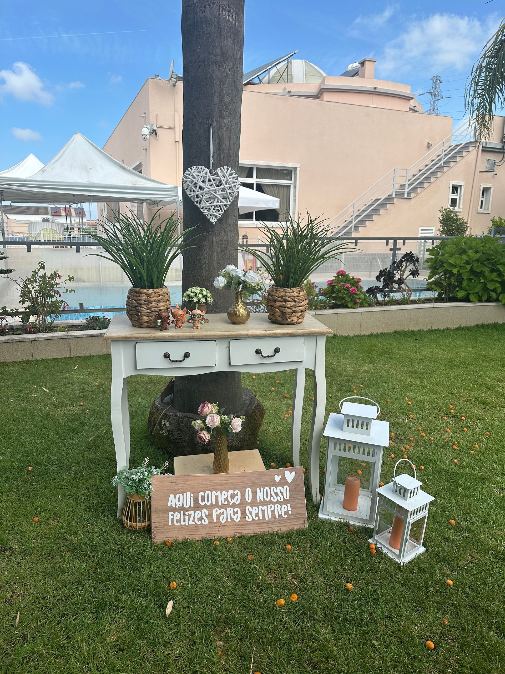 Decoración de boda con mesa, flores, faroles y cartel en un jardín.