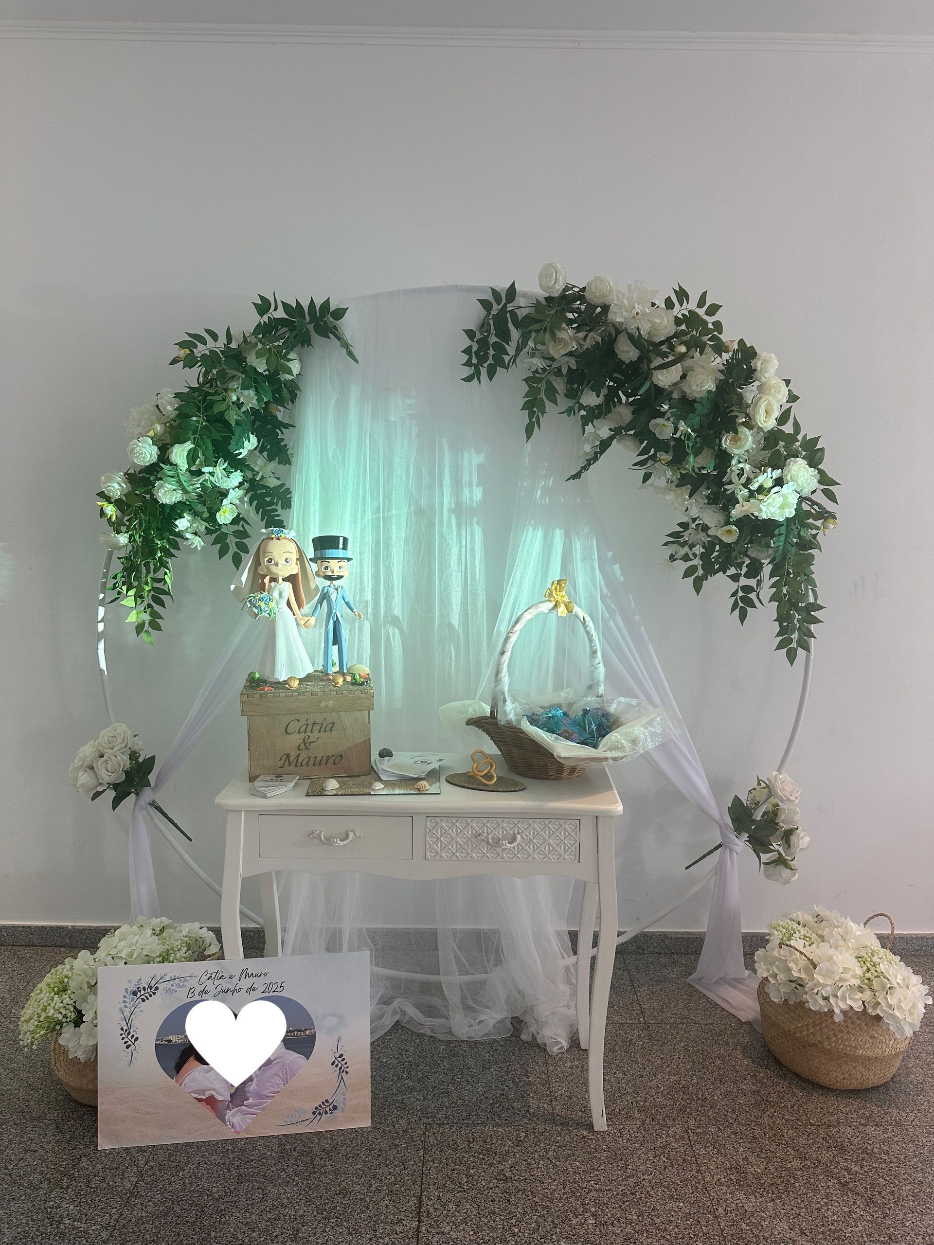 Altar nupcial con arco floral, mesa y adorno para pastel. Flores blancas y verdes, tela drapeada y cestas.