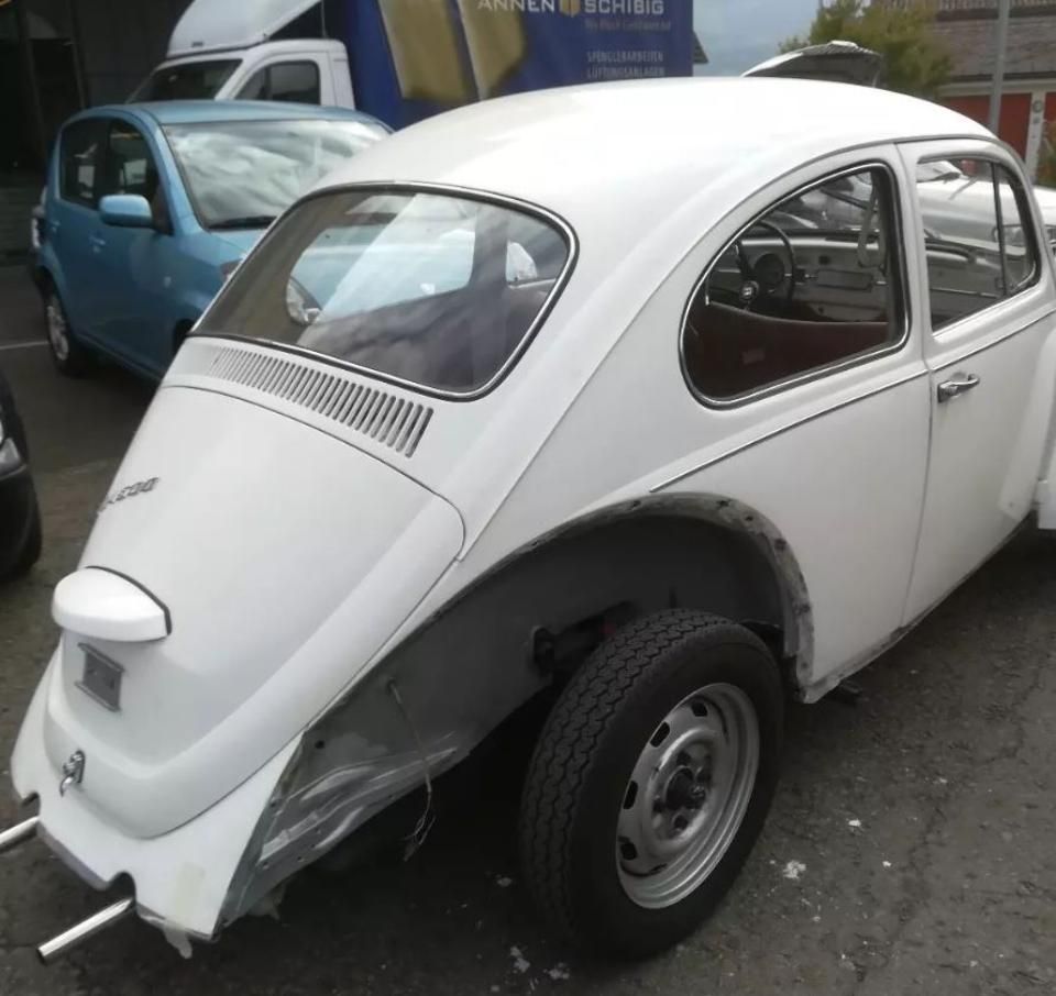 Ein weißes Auto steht auf einem Parkplatz, im Hintergrund ist ein blauer LKW zu sehen