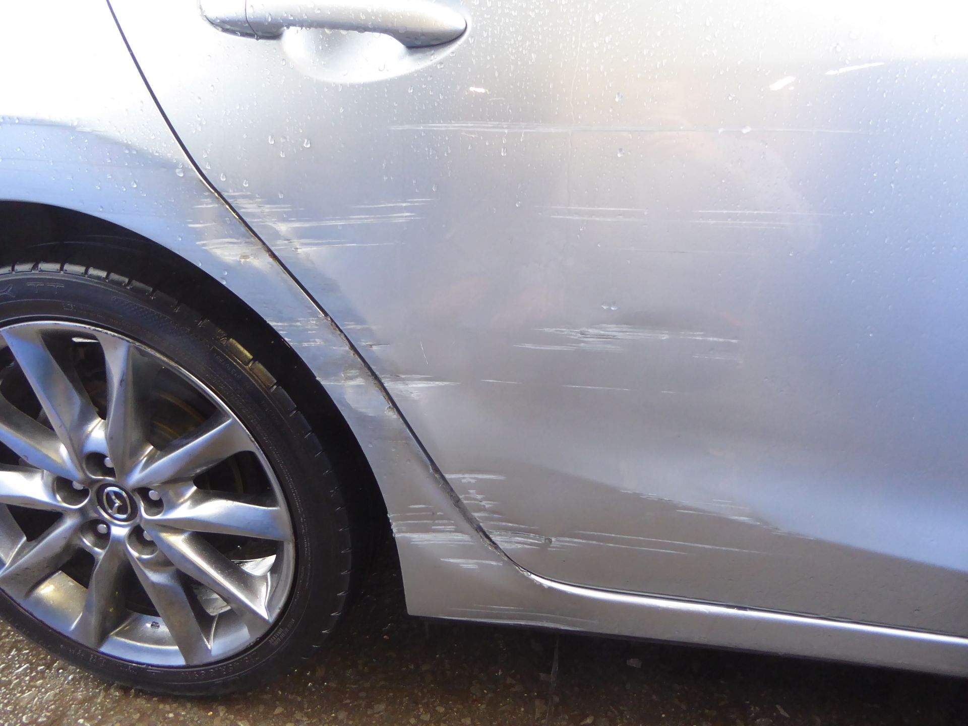 Ein silbernes Auto mit einer beschädigten Seitentür steht am Straßenrand.