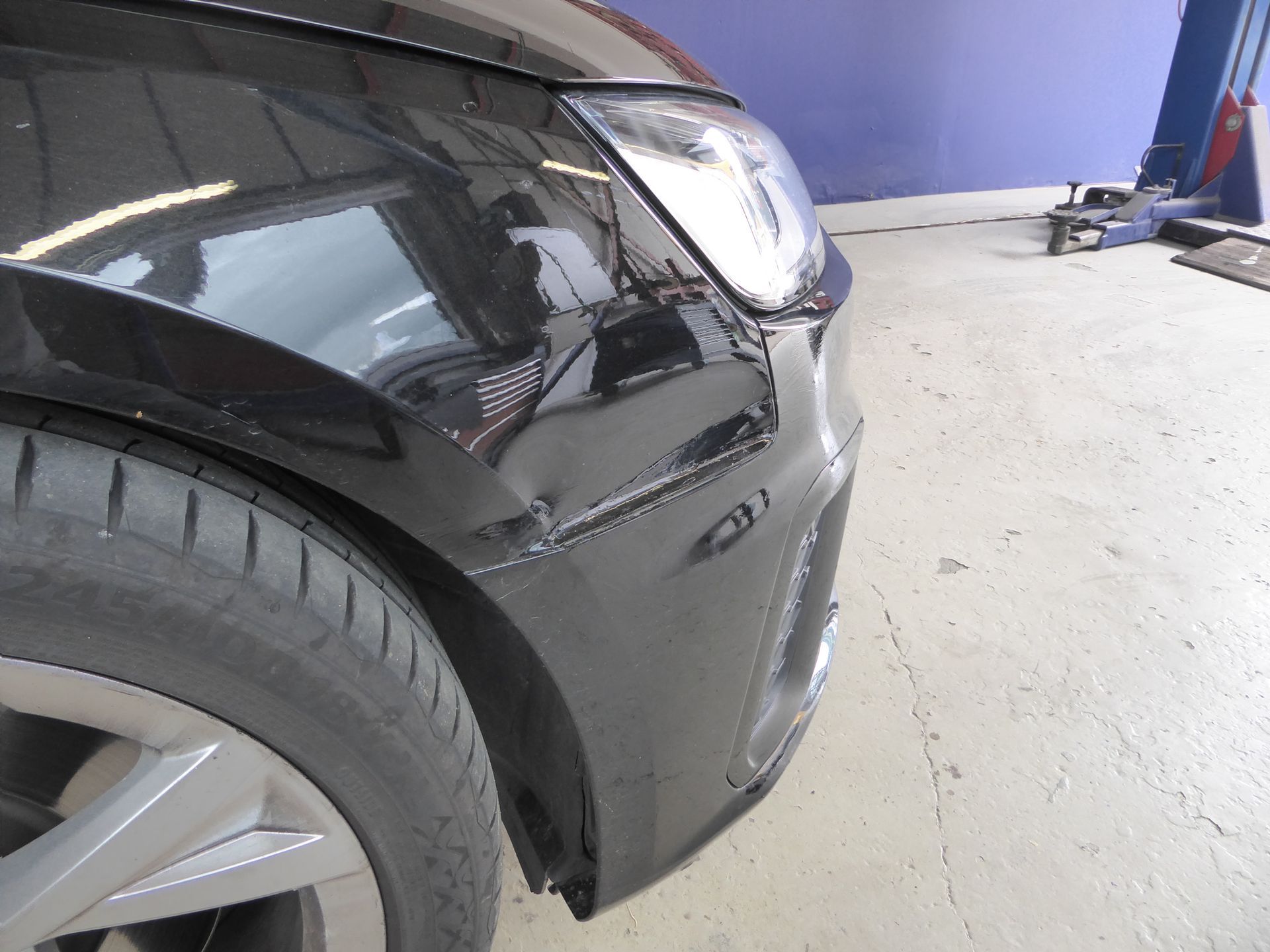 Ein schwarzes Auto mit beschädigter Stoßstange steht in einer Garage