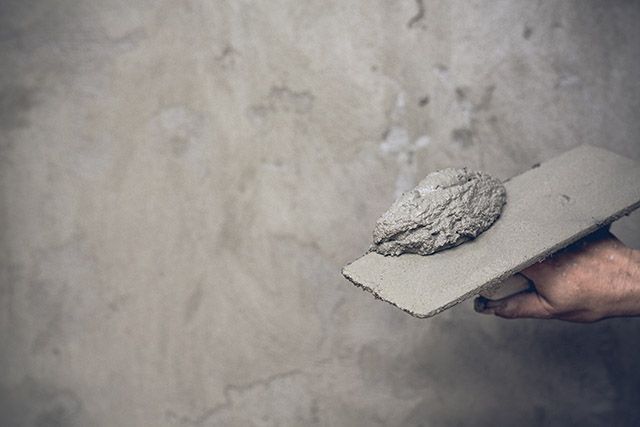 Ein Mann kniet nieder und verputzt eine Wand mit einem Spachtel.