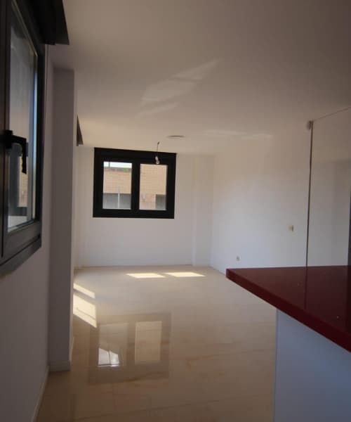 Habitación vacía con suelo beige brillante, encimera roja y ventanas con marcos oscuros.